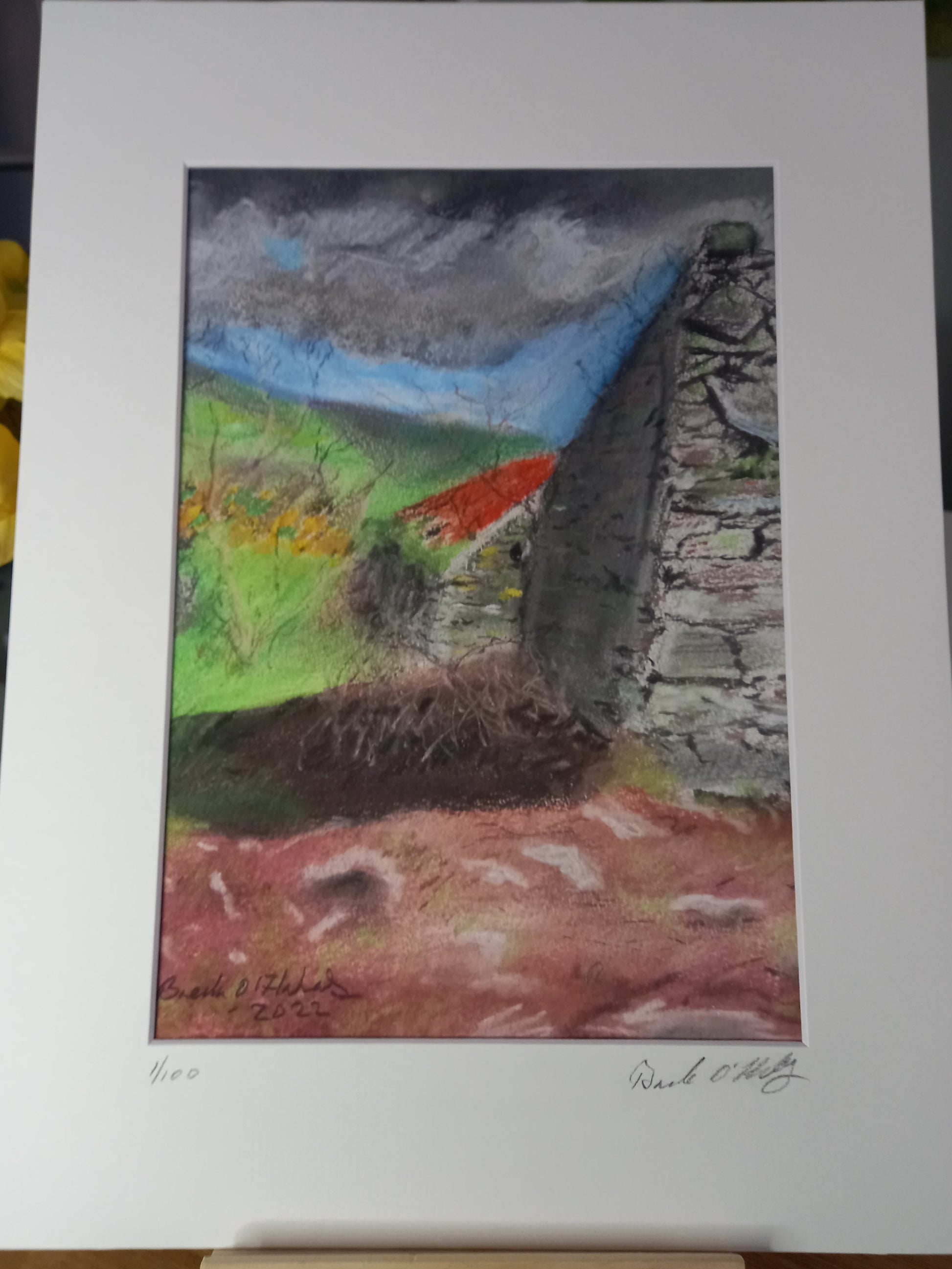 A mounted, unframed print of a pastel and colored pencil drawing depicting an abandoned village scene with old ruins, a stone wall, and a grassy field in the background.