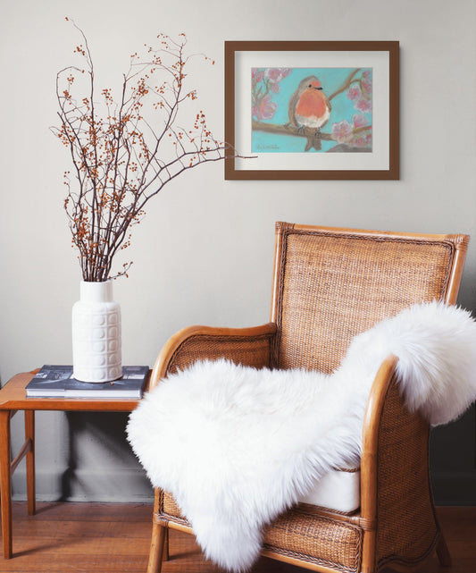 A painting of a robin amongs the cherryblossoms hangs on a light grey wall.  A wicker chair and table below it.