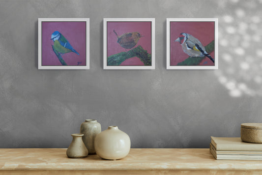a collection of three small bird paintings in a white frame hanging on a grey wall 