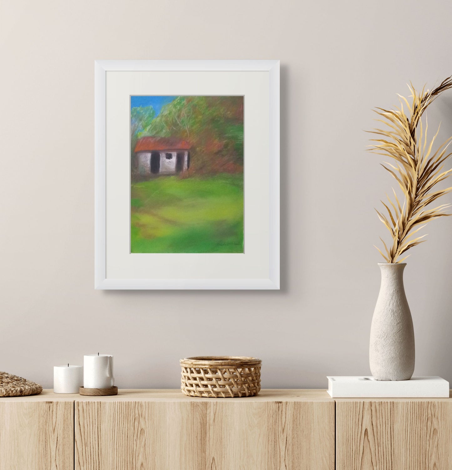 Framed painting of a landscape with a house on a wall above a wooden shelf with decorative items.